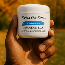 Load image into Gallery viewer, Hand holding a jar of 'Balm'd Out Butters' baby powder deodorant balm against an autumn background.
